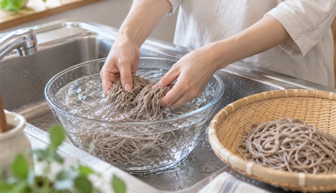 冷水を入れたボウルの中で、ゆでたそばを手で締めている様子。