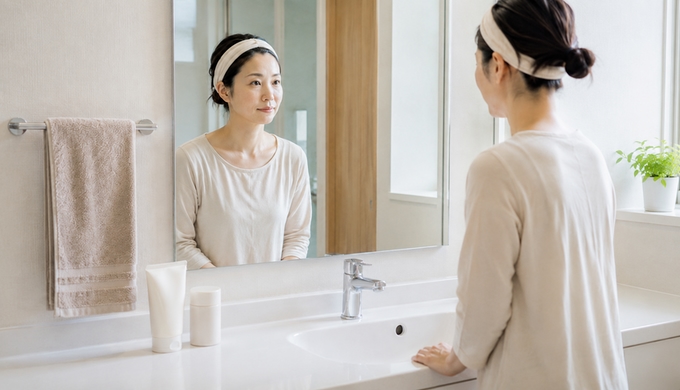 洗顔前の女性が洗面所の鏡を見ながら、洗い方を変える場所を選んでいる。