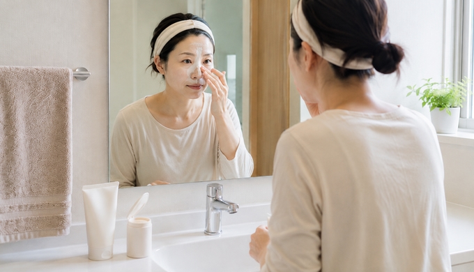 女性が洗面所でTゾーンや小鼻だけにパウダーを重ねて洗顔している。