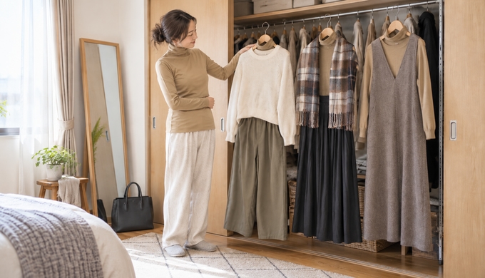 クローゼットにまとめた3つのコーデ候補を、タートルネックを着た女性が見ながら一つへ手を伸ばしている。